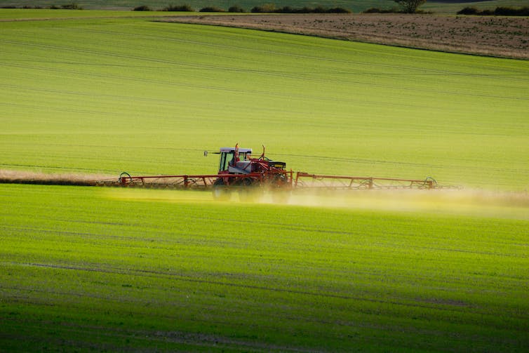 A tractor with outspread spraying arms in a field.